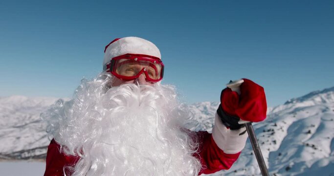Cool bearded Santa Clause wearing red skiing goggles looking around at winter snowy landscape, checking his way for tracking - christmas spirit concept 4k footage