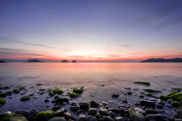 Obraz premium Amazing seashore sunrising,endless horising and green mossy round gravel pebble beach, sea waves beats on a rocky shore with foam.