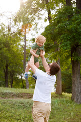 Young father and little son. Dad throws his son up against the background trees. Walk in park. Family life.