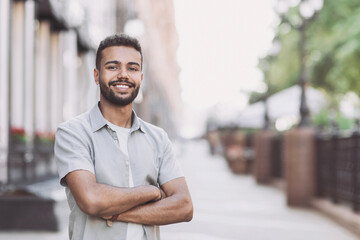 Handsome smiling young man portrait. Cheerful men with crossed arms looking at camera in city....