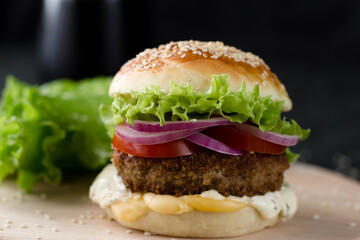 A homemade hamburger is sitting on a wooden shelf, next to a glass of coke