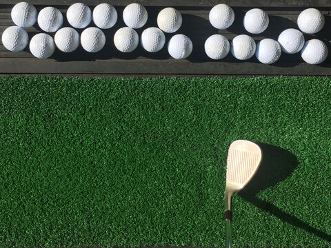 Group of golf ball in rubber tray with wedge iron club on practice grass mat under morning sunlight top view