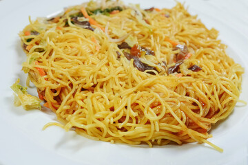 Simple chicken chow mein meal on a white plate and on a wooden table. Chinese stye tasty noodles with sauce and vegetables. Concept dinner, Asian flavor.