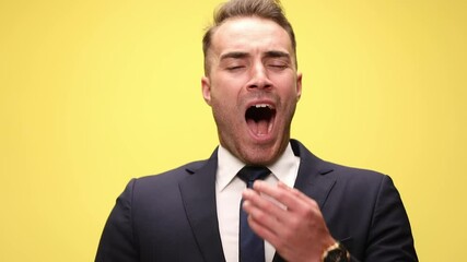 sleepy young businessman in suit opening mouth and yawning, covering mouth with hand and smiling on yellow background - Powered by Adobe