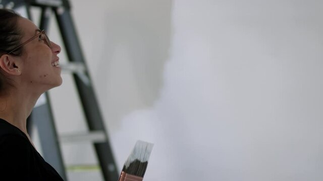 Woman painting room stops to admire work - side profile