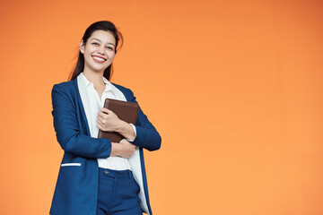 Portrait of lovely young female entrepreneur with tablet computer posing against orange background