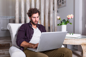 Man using laptop computer, working at home. Worried about finances. Handsome man with beard working at home on project, he is sitting on sofa looking at his laptop in front of him. Focus on the man