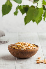 Salted peanuts in a wooden bowl on a light wooden table with green leaves in the background. Healthy snacks. Nuts.