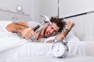 Obraz na płótnie Canvas Young man tries to break the alarm clock with hammer, Destroy the Clock. Man lying in bed turning off an alarm clock with hammer in the morning at 7am.