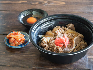 プラスチック容器に入った紅生姜が乗った牛丼と生卵とキムチ。
