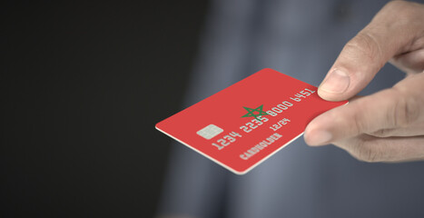 Man offers plastic bank card with printed flag of Morocco. Fictional numbers