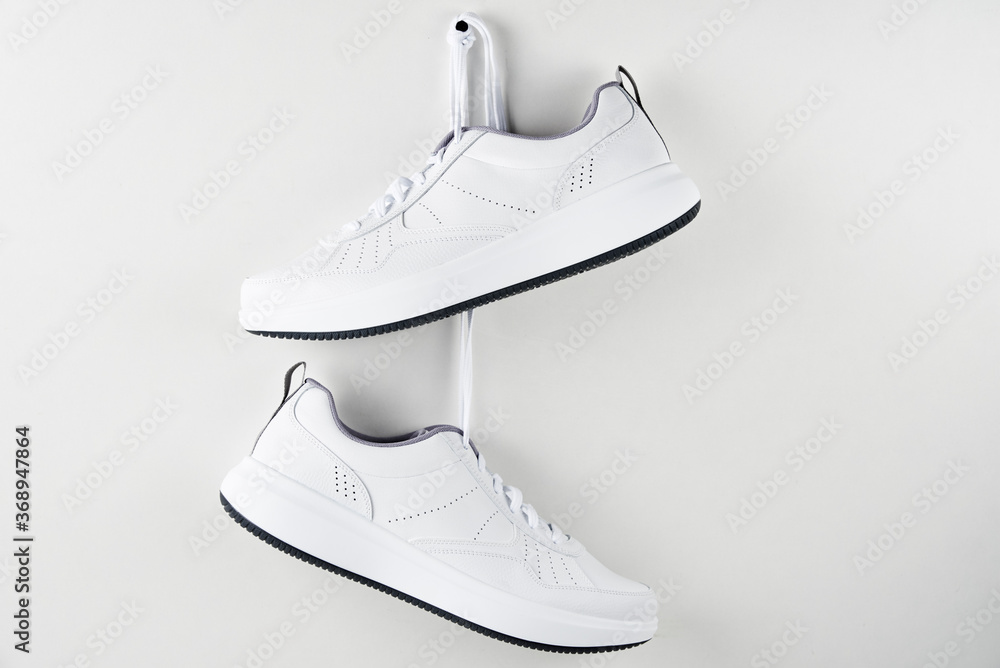 Wall mural Pair of white male sneakers hanging on wall. Fashion stylish sport shoes, close up