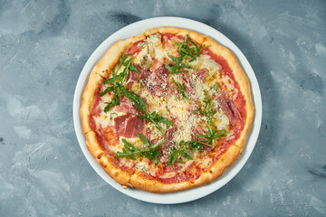 Homemade pizza with jamon, arugula and parmesan in a white plate on a concrete background. Close up. Selective focus