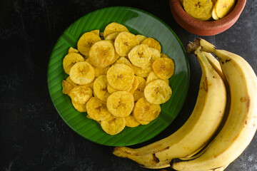 Kerala snack Banana chips or Kaya Varuthathu fried snack in terracotta, clay pot on dark background...