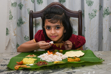 Kerala Onam festival, happy Indian girl child eating Onam sadhya with hand wearing traditional...