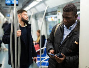 Fototapeta na wymiar African American man browsing and typing messages on phone on way to work in modern metro car