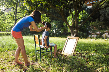 A woman cuts the hair of a child in the yard of the house during quarantine.