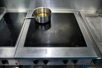 Industrial kitchen induction hub with a pot of oil. Stainless-steel material and black cooking surface. High-quality photo