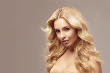 Blonde caucasian woman has long hair, beauty portrait of female face with natural skin on isolated light brown background.
