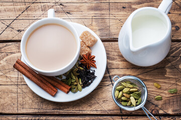 Indian drink masala tea with milk and spices. Cardamom sticks cinnamon star anise cane sugar. Wooden background copy space.