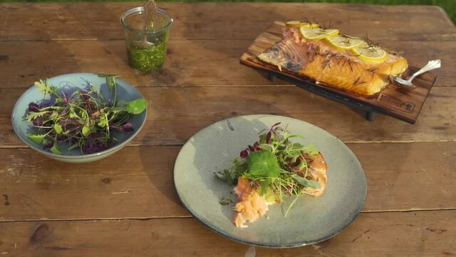 Professionally grilled salmon on wooden plate with lemon, next to it beautifully served piece of salmon with cress, greens and homemade pesto. SLOW MOTION 50 fps.