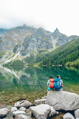 Fototapeta premium Morske Oko, Poland - September 12, 2019: hikers couple sitting on rock looking at lake in mountains