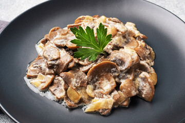 Stewed mushrooms champignons in sauce with sour cream and cheese parsley on a plate.