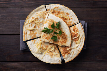 Pieces of quesadilla with mushrooms sour cream and cheese on a plate with parsley leaves. Wooden...