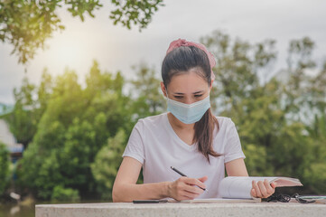 Fototapeta premium Asian women a wearing face mask reading book sitting outdoor at University