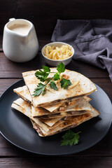 Pieces of quesadilla with mushrooms sour cream and cheese on a plate with parsley leaves. Wooden background copy space.