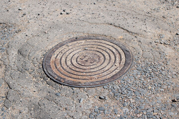 Round manhole on old asphalt in sand