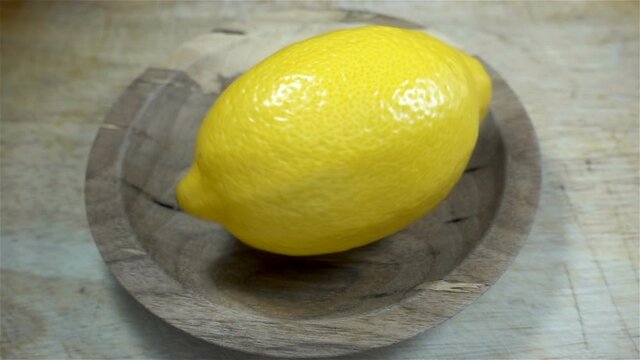 One lemon rotates in slow motion on a wooden background