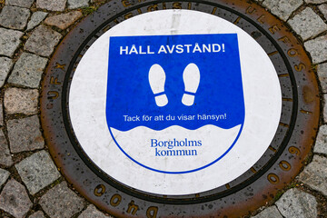 Borgholm, Oland, Sweden A man hole cover with a "keep your distance sign."