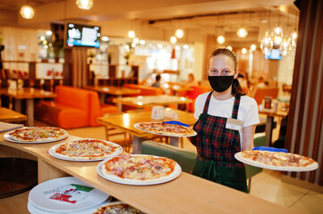 Waiter in protective mask hold pizza in pizzeria.