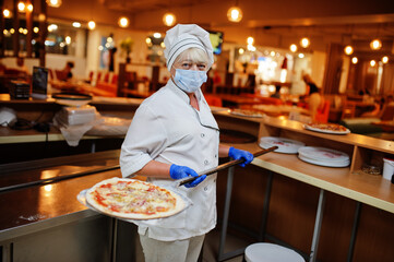 Pizza maker in protective mask working in the pizzeria.