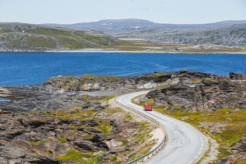 Fototapeta premium A red parcel delivery van on winding road in northern Norway in summer