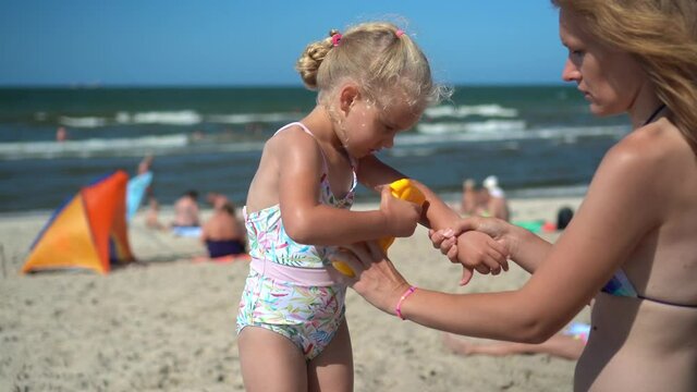 Beautiful mom help her little daughter girl apply sunscreen cream on hands