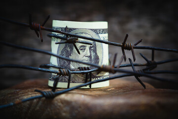 Fototapeta na wymiar Barbed wire against US Dollar bill as symbol of economic warfare, confrontation, sanctions and embargo busting.