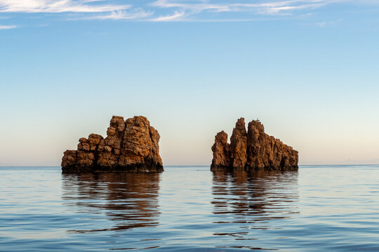 Nes Portes Rocks with a cross on top, north of Paros Island sticking out from perfectly flat calm Mediterranean Sea during early windless morning, Greece.