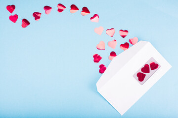 Red confetti hearts fly out of a white envelope on a light blue background. Valentine's Day. love concept Gift, message for lover