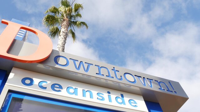 Oceanside nameboard sign and palm trees. Oside is the popular american tourist resort, pacific ocean west coast, San Diego County, California USA. Name of city of vacations and tourism on coastline
