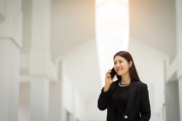 Portrait of a young Asian business woman talking over cellphone and holding cup of coffee in business building. Photo of beautiful girl in casual suite with phone and cup of coffee. stock photo