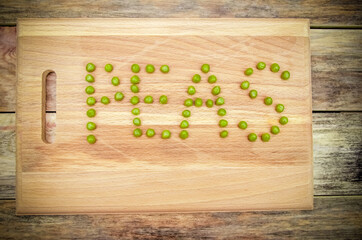 word pea is written in green pea seeds on a wooden Board on a wooden background