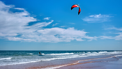Man kitesurfing or kite boarding sports on Brora beach in the Highlands on a sunny day with blue skies