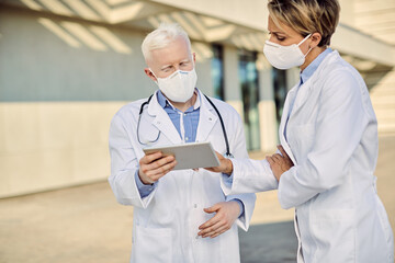 Doctors with protective face masks cooperating while using touchpad outdoors.