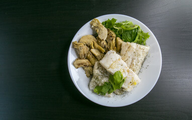Hake fish with artichokes, parsley, fine herbs and green salad with olive oil. Top view