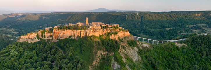 Fototapeta na wymiar Civita di Bagnoregio. Panoramic, aerial view of Italian ancient village standing on rock plateau, illuminated by setting sun. City on rock over Tiber river valley. Italy.