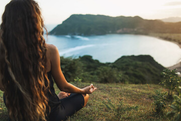 Woman meditating yoga alone at sunrise mountains. View from behind. Travel Lifestyle spiritual relaxation concept. Harmony with nature. - obrazy, fototapety, plakaty