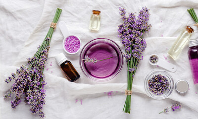 Lavender oils, liquids, parfumes, lavender flowers on white fabric. Set skincare spa beauty...