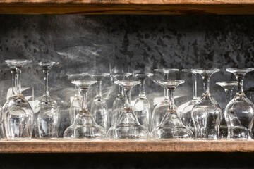 Set of different champagne, wine, martini empty clean glasses on bar restaurant wooden shelf. Gray concrete wall, loft interior design. Shining sun light.